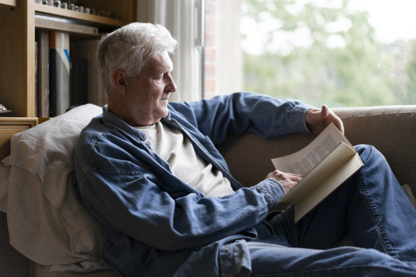 starszy mezczyzna czytajacy ksiazke podczas relaksu