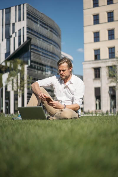 biznesmen z laptopem siedzacy w trawie